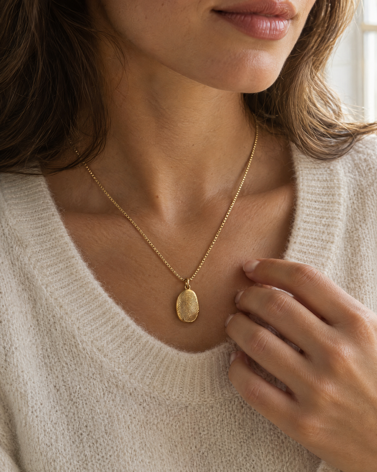 Gold fingerprint necklace on a box chain, worn with a cream sweater