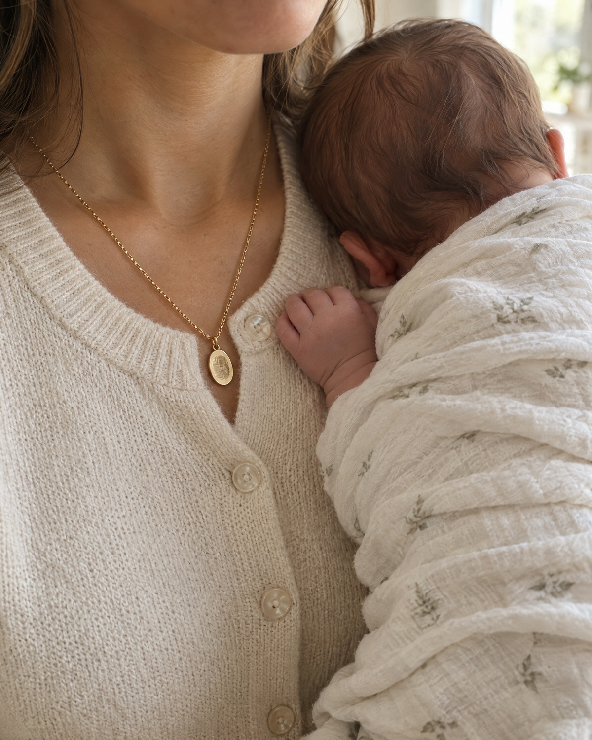 Mother holding her newborn, wearing a gold fingerprint necklace