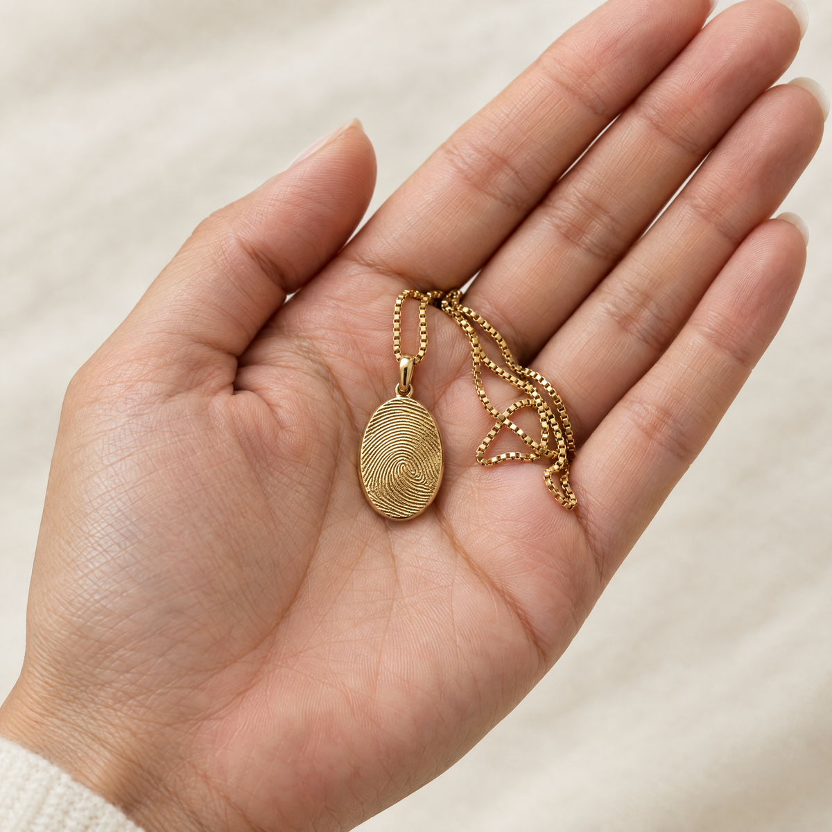 Gold fingerprint pendant resting in an open palm to show its size